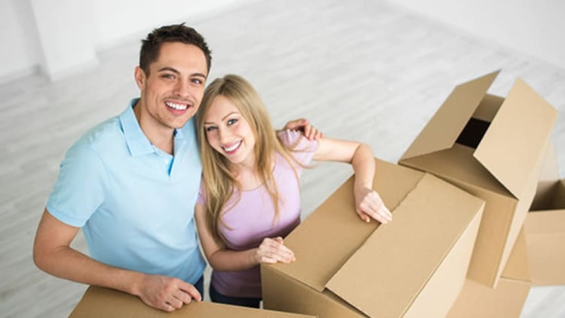 Couple leaning on packed moving boxes in an empty room of their new home